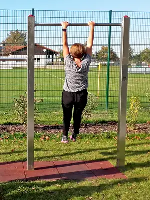 Photo of a young woman practising unhooking on the horizontal bar, looking onto a football pitch