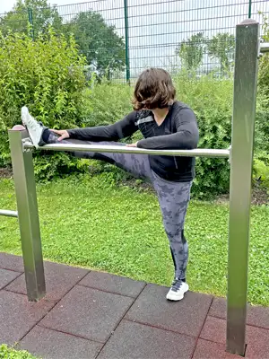 Training Calisthenics-Anlage Photo of a young woman training stretching on the horizontal bar, behind her everything is beautifully green.