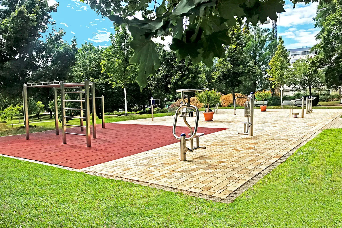 Fitnessgeräte für Körpertraining im Freien, umgeben von Bäumen im Park.